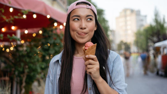 Belle femme asiatique mangeant la crème glacée sur la rue. Hipster émotif utilisant des vêtements occasionnels retenant le dessert savoureux d’été regardant loin à l’extérieur. Fête de la nourriture